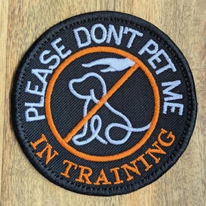 May include: A circular black patch with white text saying "PLEASE DON'T PET ME IN TRAINING". It has an orange circle with a dog silhouette and a line through it, indicating the dog is in training.