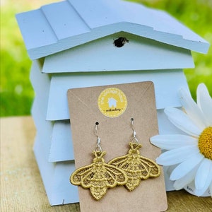 May include: A pair of gold embroidered bee earrings on a brown card with the text "the vintage haus - embroidery".