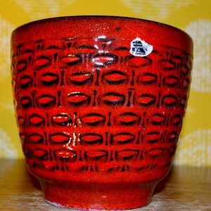 May include: Red ceramic planter with a black geometric pattern. The planter has a sticker on the side that says "A.A."