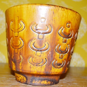 May include: A brown ceramic planter with a geometric pattern. The planter has a wide mouth and a rounded bottom.