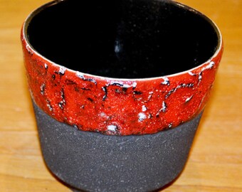 May include: A black and red ceramic planter with a textured finish. The planter has a wide, round opening and a slightly flared base.