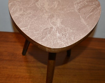 May include: A small, triangular table with a light pink, marbled top and three dark brown legs.