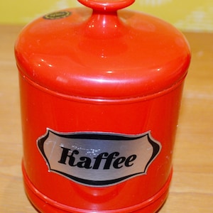 Peut inclure: Une boîte à café en céramique rouge avec une étiquette argentée qui indique "Kaffee".