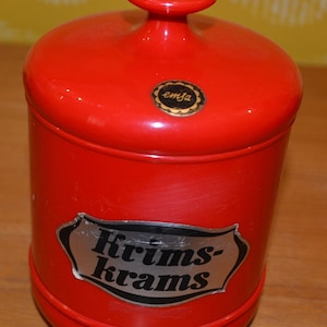 Peut inclure: Pot en céramique rouge avec un couvercle et une étiquette argentée indiquant "Krims-Krams". Le pot a un autocollant noir et or indiquant "emsa" sur le couvercle.