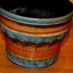 Op de afbeelding: Een bruine en blauwe keramische plantenpot met een decoratief ontwerp. De pot heeft een brede rand en een afgeronde bodem.