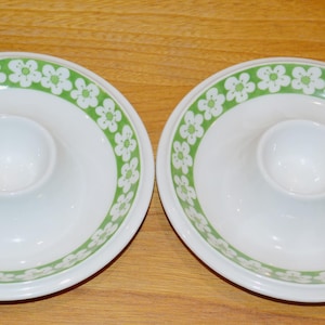 Könnte beinhalten: Zwei weiße Eierbecher aus Keramik mit grünem und weißem Blumendesign. Die Becher haben eine erhöhte Mitte zum Halten eines Eies.