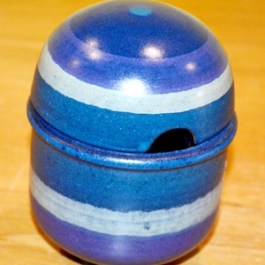May include: A blue and white ceramic sugar bowl with a lid. The bowl has a striped pattern and a small hole in the lid.