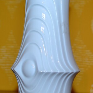Puede incluir: Jarr&oacute;n de cer&aacute;mica blanco con un dise&ntilde;o ondulado y abstracto. El jarr&oacute;n tiene un acabado liso y brillante.