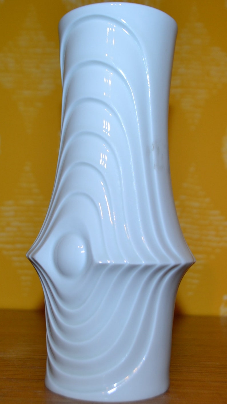 Puede incluir: Jarr&oacute;n de cer&aacute;mica blanco con un dise&ntilde;o ondulado y abstracto. El jarr&oacute;n tiene un acabado liso y brillante.
