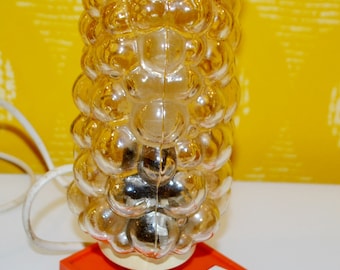 May include: A vintage table lamp with a clear glass shade featuring a bubbled texture. The lamp has a red base with a white toggle switch.