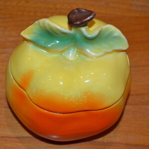 Könnte beinhalten: Eine orangefarbene, keramik-geformte Schale in Form einer Frucht mit einem grünen Blatt und einem braunen Stiel oben. Die Schale ist in Gelb und Orange glasiert.
