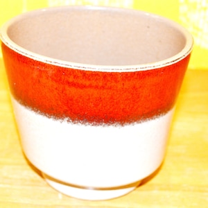 May include: A brown and white ceramic planter with a red band around the middle.