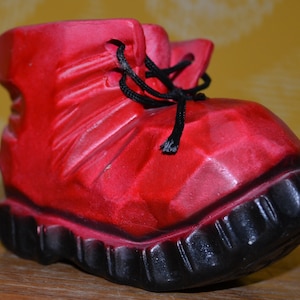 May include: A red, rubber, boot-shaped planter with a black rubber sole. The planter has a textured surface and a lace-up design.