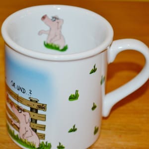 Puede incluir: Taza de cerámica blanca con un diseño de cerdo de dibujos animados. La taza tiene un fondo azul y blanco con hierba verde y una valla de madera. El texto en la taza dice "Ja. Und...?"