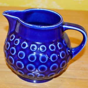 May include: A cobalt blue ceramic creamer with a textured surface of small circles. The creamer has a rounded body and a handle.