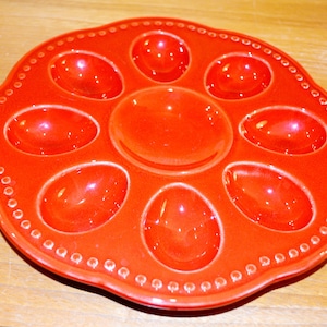 Pode incluir: Um prato de ovos de cerâmica vermelha com oito reentrâncias individuais para servir ovos recheados ou outros aperitivos.