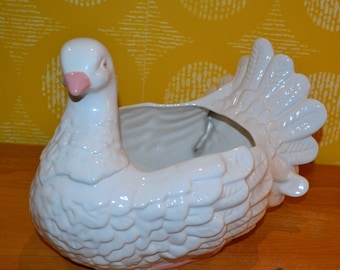 May include: White ceramic planter shaped like a turkey with a pink beak. The planter has a textured surface and is designed to hold plants.