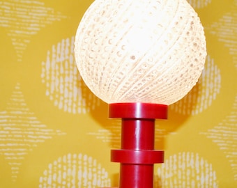 May include: A red and white table lamp with a textured white glass shade. The lamp has a round base and a cylindrical stem.