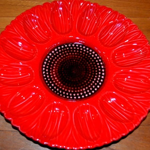 May include: A red ceramic serving dish with 12 individual sections, ideal for serving snacks or devilled eggs. The centre of the dish features a black and white polka dot design.