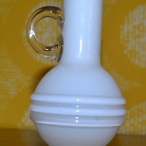 May include: A white ceramic vase with a rounded body and a single handle. The vase has a textured, ribbed design and a clear glass base.