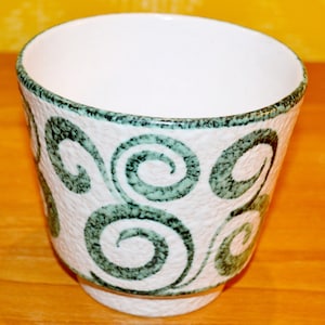 May include: White ceramic planter with a green swirl design. The planter has a textured surface.