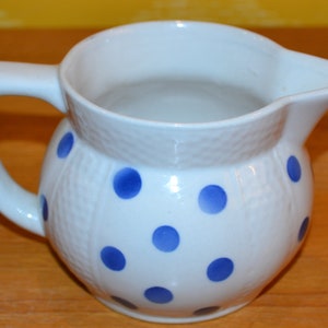 May include: White ceramic pitcher with a blue polka dot pattern. The pitcher has a handle and a rounded body.