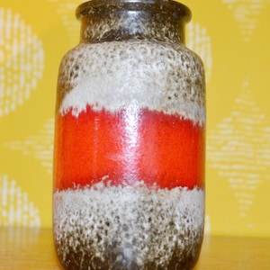 Puede incluir: Un jarrón de cerámica con un esmalte marrón, blanco y rojo. El jarrón tiene un patrón moteado y un cuerpo ancho y redondo.