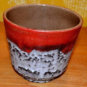 Könnte beinhalten: Ein Keramik-Pflanztopf mit strukturierter Oberfläche. Die Oberseite ist leuchtend rot, geht in Weiß und Schwarz über. Der Innenraum ist warmbraun. Dieser dekorative Pflanztopf ist für Zimmerpflanzen geeignet.
