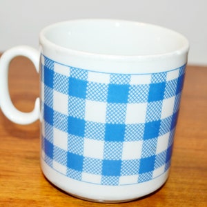 Könnte beinhalten: Weiße Keramiktasse mit einem blau-weiß karierten Muster.