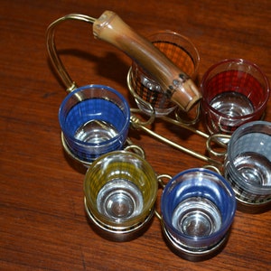 May include: A set of six colorful shot glasses with a gold metal stand and a wooden handle. The glasses have a checkered pattern in blue, yellow, red, and orange.