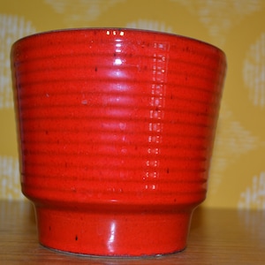 May include: A red ceramic planter with a ribbed design. The planter is glazed and has a shiny finish.