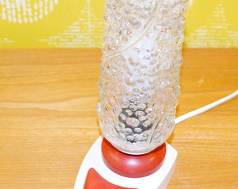 May include: A white table lamp with a clear glass shade featuring a textured bubble design. The lamp has a red switch and a white cord.