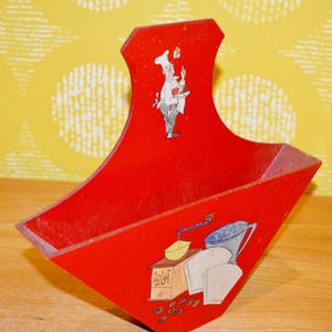 Könnte beinhalten: Ein roter Küchenhelfer aus Holz mit Griff. Der Küchenhelfer zeigt eine Kochillustration und ein Kaffeemotiv mit Kaffeemühle und Bohnen. Er dient wahrscheinlich zum Aufbewahren von Küchenutensilien oder Vorräten.