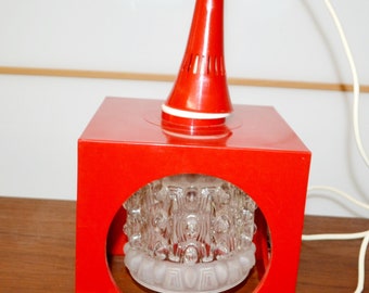 May include: A red metal pendant light fixture with a clear glass shade. The shade has a textured, geometric design. The fixture has a white cord.