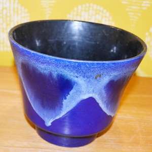 May include: A blue and white ceramic planter with a black interior. The planter has a wide, round opening and a narrow base.