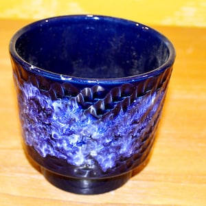 May include: A blue ceramic planter with a white marbled design. The planter has a textured, wavy rim.