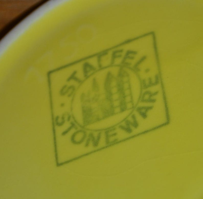 K&ouml;nnte beinhalten: Ein gr&uuml;ner Stempel auf gelbem Hintergrund mit dem Text "Stafford Stoneware" und einem stilisierten Bild eines Geb&auml;udes.