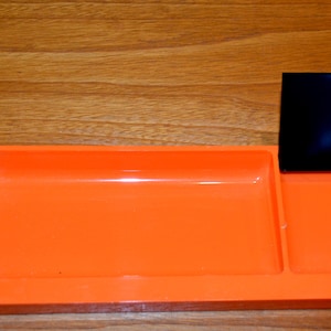 May include: An orange plastic desk organiser with two compartments. The organiser has a black plastic divider.