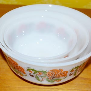 Könnte beinhalten: Set aus drei weißen, ineinander verschachtelten Schalen mit Blumenmuster. Die Schalen haben orange, grüne und braune Blumen auf weißem Hintergrund.