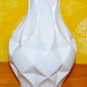 May include: A white ceramic vase with a geometric design. The vase has a wide mouth and a rounded base.