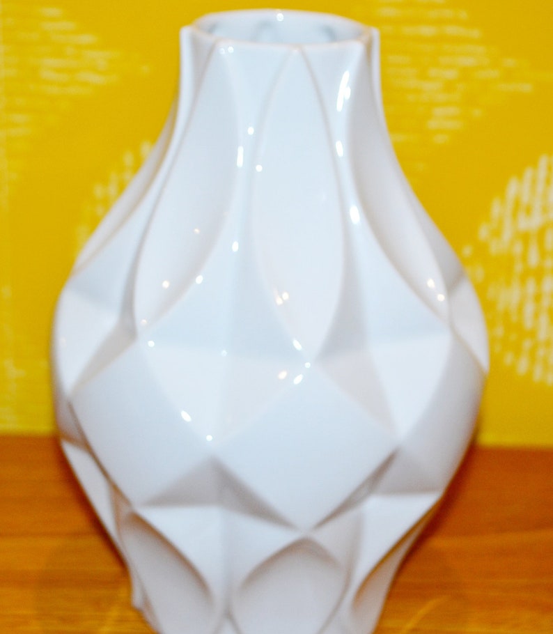 May include: A white ceramic vase with a geometric design. The vase has a wide mouth and a rounded base.