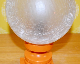 May include: A vintage orange table lamp with a frosted glass globe shade. The lamp has a textured, cracked glass shade and a base with a stacked, cylindrical design.
