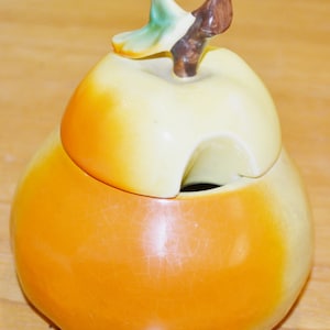 Peut inclure: Un sucrier en céramique en forme de poire avec un couvercle. Le couvercle est en forme de poire avec une feuille verte et une tige brune. Le bol est orange et le couvercle est jaune.
