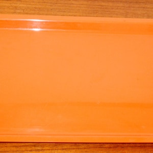 May include: A rectangular serving tray with a smooth, glossy finish in a vibrant orange color. The tray features a flat base and a slightly raised rim around the entire perimeter, providing a simple and functional design for carrying items.