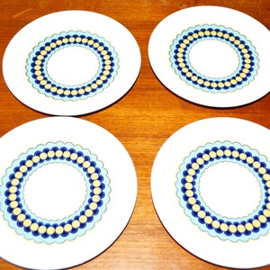 May include: Four white ceramic plates with a blue and yellow circular design. Each plate has a white center circle surrounded by a blue and yellow ring.