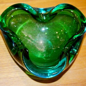 Può includere: Un portacenere di vetro verde a forma di cuore con un bordo ondulato.