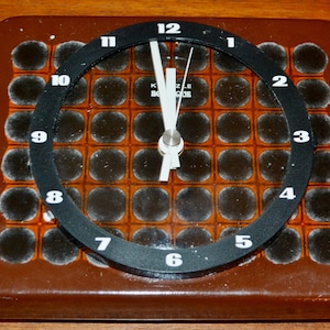 May include: A square brown clock with a black face and white numbers. The clock has a grid pattern of black and orange squares.