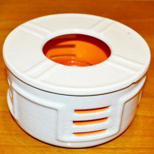 Può includere: Scaldabiberon in ceramica bianca con un anello interno arancione e tre linee orizzontali arancioni sul lato.