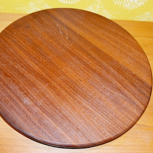 Puede incluir: Una mesa redonda de madera con un acabado marrón intenso. La superficie muestra la veta natural de la madera y algunos pequeños arañazos. La mesa está sobre un fondo amarillo y de madera.