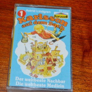 Può includere: Una musicassetta vintage con il titolo "Karlsson auf dem Dach" di Astrid Lindgren. La copertina raffigura un bambino dei cartoni animati che vola sopra una città. La cassetta è in un astuccio di plastica trasparente, con testo in tedesco.